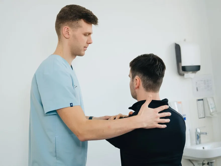Remedial massage therapist treating a client's shoulders in a bright clinic room